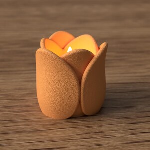 May include: A peach-colored candle holder shaped like a tulip flower. The candle holder has a textured surface and contains a lit candle, emitting a warm glow. The background is a wooden surface.