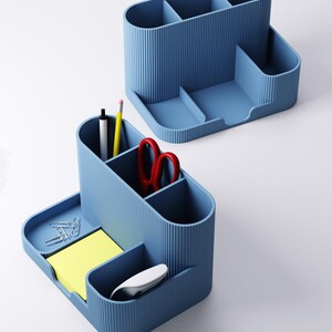 May include: Two blue desk tidies with multiple compartments. One tidy contains a pen, pencil, and red scissors. The other has paperclips, sticky notes, and a computer mouse. Both tidies have a ribbed texture.