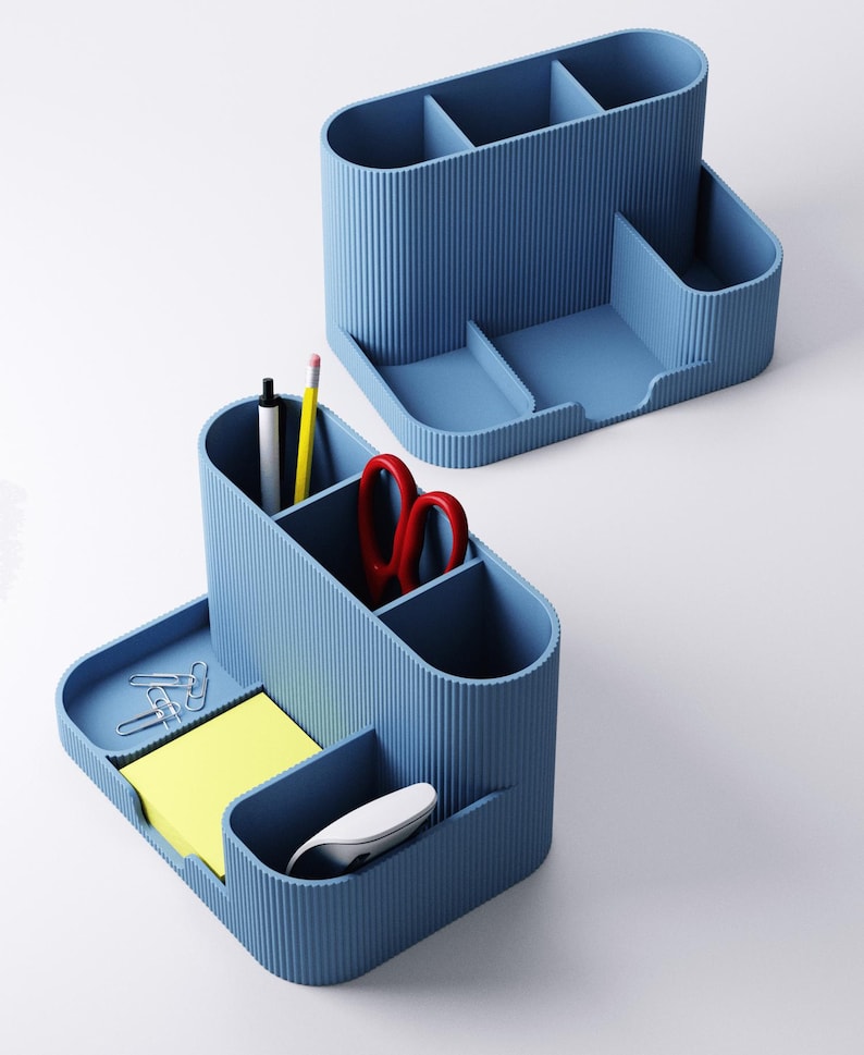 May include: Two blue desk tidies with multiple compartments. One tidy contains a pen, pencil, and red scissors. The other has paperclips, sticky notes, and a computer mouse. Both tidies have a ribbed texture.