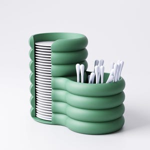 May include: A green, modern kitchen organizer with a stacked design. It features a section for plates and a separate compartment holding white utensils. The organizer has a unique, wavy structure and a minimalist aesthetic.
