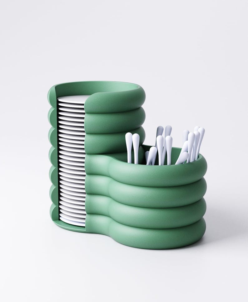 May include: A green, modern kitchen organizer with a stacked design. It features a section for plates and a separate compartment holding white utensils. The organizer has a unique, wavy structure and a minimalist aesthetic.
