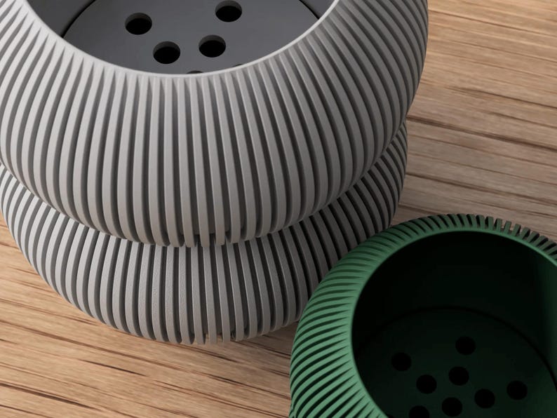 May include: Three modern, ribbed planters in shades of gray and green. The gray planters are stacked, showcasing a detailed, grooved design. The green planter is positioned to the side, offering a contrasting color and texture. The planters sit on a wooden surface.