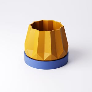 May include: A geometric yellow planter with a faceted design sits atop a blue circular base. The planter has a wide, open top and a textured, angular exterior. The design is modern and minimalist.