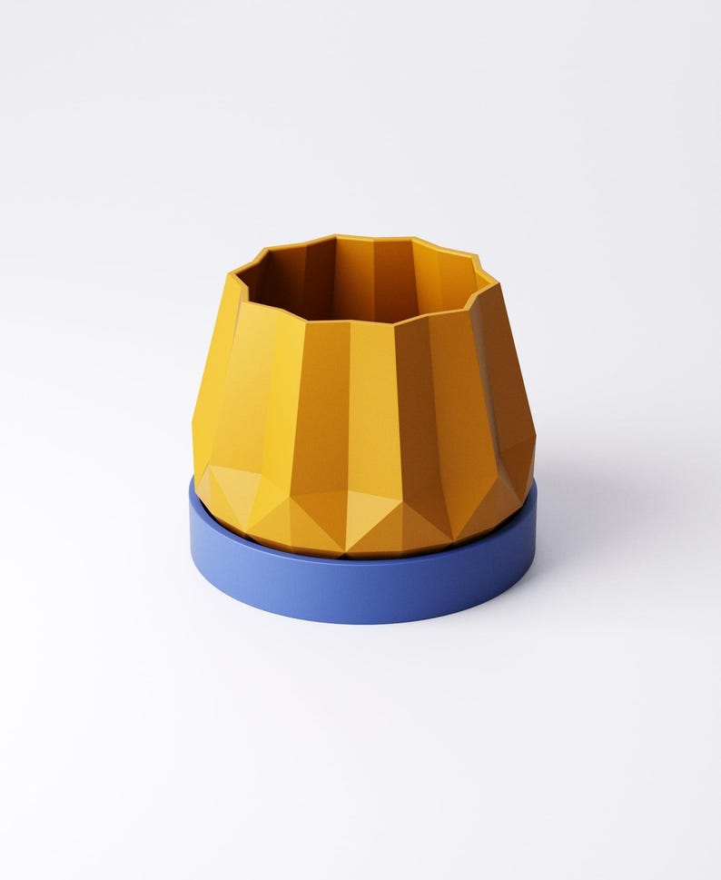 May include: A geometric yellow planter with a faceted design sits atop a blue circular base. The planter has a wide, open top and a textured, angular exterior. The design is modern and minimalist.