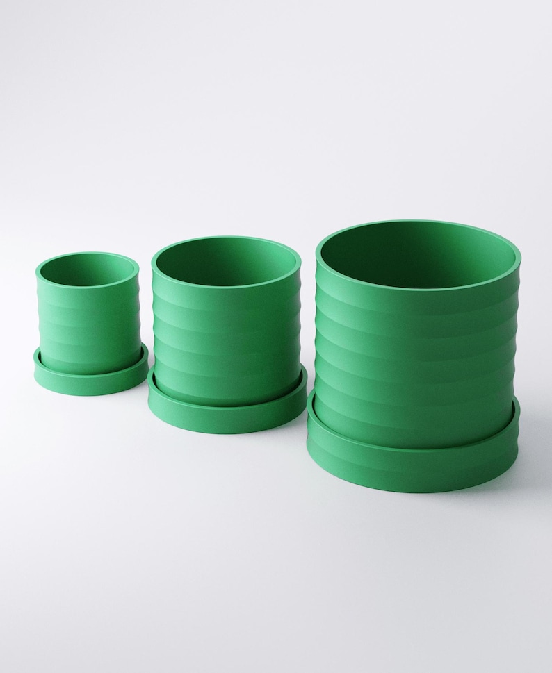 Op de afbeelding: Drie groene cilindrische bloempotten van verschillende formaten, elk met een bijpassende schotel. De potten hebben een geribbeld ontwerp aan de buitenkant. De kleinste pot is ongeveer 10 cm hoog, de middelste pot 15 cm en de grootste 20 cm.