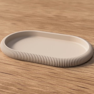 Puede incluir: Una bandeja ovalada beige con borde acanalado. La bandeja est&aacute; hecha de un material s&oacute;lido y se coloca sobre una superficie de madera. El dise&ntilde;o es minimalista y moderno, adecuado para la decoraci&oacute;n del hogar o para servir.