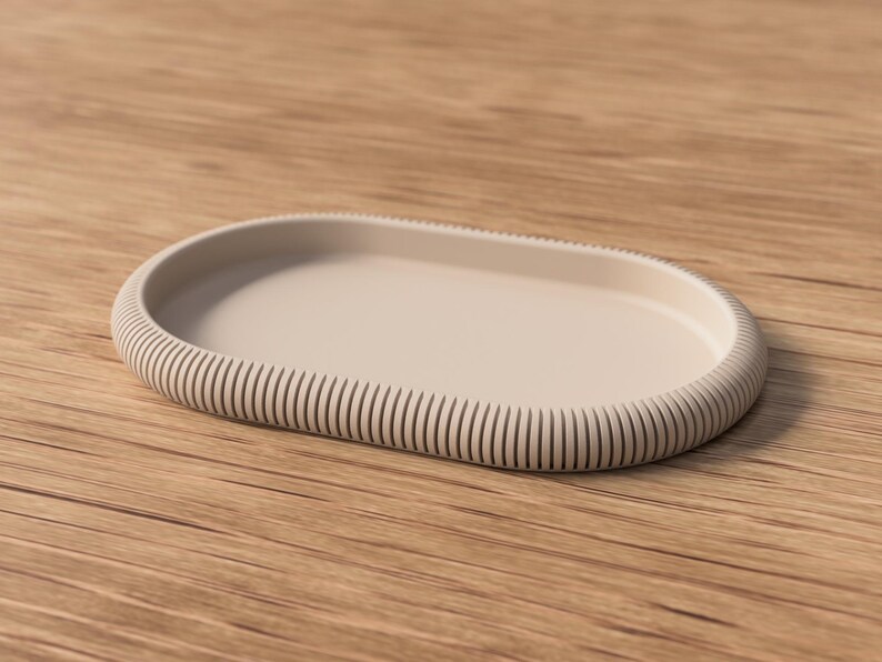 Puede incluir: Una bandeja ovalada beige con borde acanalado. La bandeja est&aacute; hecha de un material s&oacute;lido y se coloca sobre una superficie de madera. El dise&ntilde;o es minimalista y moderno, adecuado para la decoraci&oacute;n del hogar o para servir.