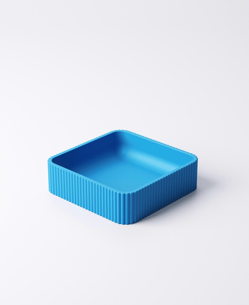 May include: A bright blue, square container with a ribbed exterior. The container has a simple, modern design and is likely made of plastic or a similar material. The interior is smooth and empty.