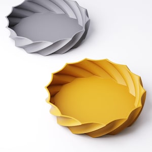May include: Two decorative trays with a spiral design. One tray is gray, and the other is yellow. The trays have a round shape with a wavy, textured edge. The trays are on a white background.