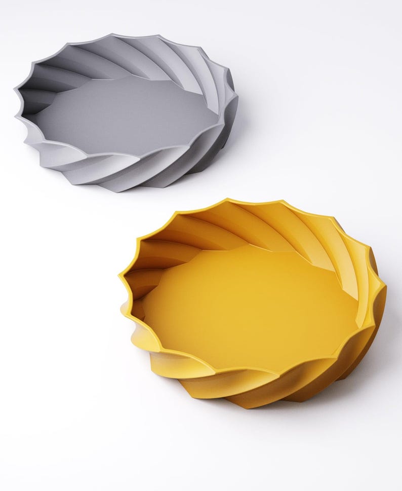 May include: Two decorative trays with a spiral design. One tray is gray, and the other is yellow. The trays have a round shape with a wavy, textured edge. The trays are on a white background.
