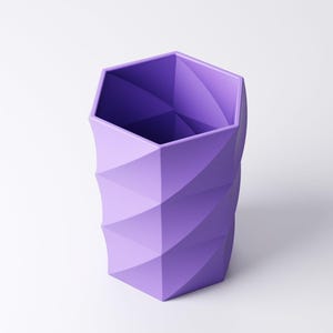 May include: A geometric, purple pencil holder with a hexagonal top and a spiraling, textured design. The container is made of a solid material and is set against a white background. The pencil holder is approximately 5 inches tall.