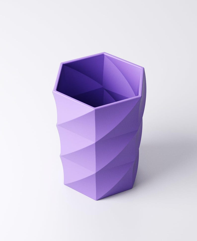 May include: A geometric, purple pencil holder with a hexagonal top and a spiraling, textured design. The container is made of a solid material and is set against a white background. The pencil holder is approximately 5 inches tall.