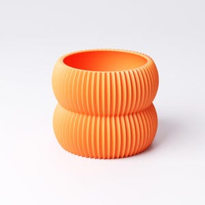 May include: An orange, ribbed, two-tiered planter. The cylindrical pot has a rounded base and top, with vertical ridges creating a textured surface. The interior is smooth and the color is a vibrant, solid orange.