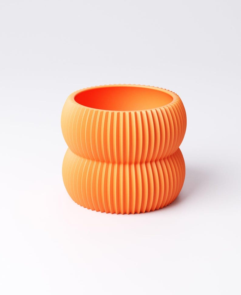 May include: An orange, ribbed, two-tiered planter. The cylindrical pot has a rounded base and top, with vertical ridges creating a textured surface. The interior is smooth and the color is a vibrant, solid orange.