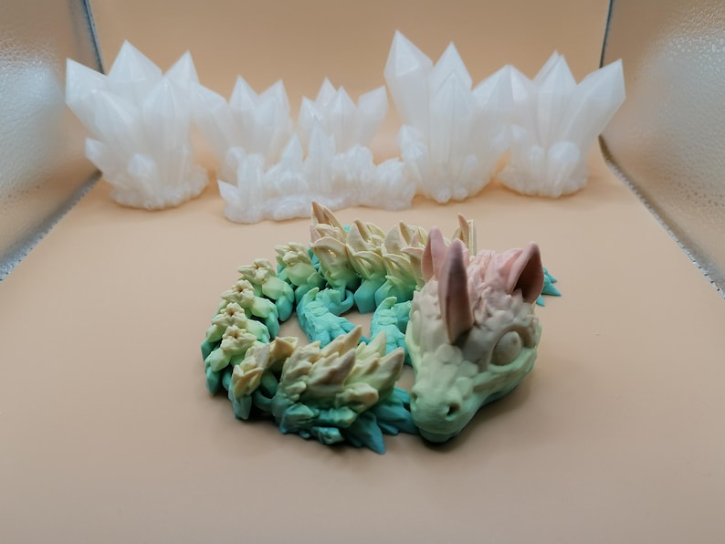 Puede incluir: Una figura de drag&oacute;n en espiral multicolor con un degradado de tonos verdes, azules y amarillos. La cabeza del drag&oacute;n es de color rosa p&aacute;lido y verde. En el fondo hay varias formaciones de cristales blancos.