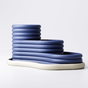 May include: A modern, blue ceramic decorative object with a tiered design. The object features a series of stacked, rounded forms in varying heights, resting on a white base. The overall shape is geometric and sculptural, suitable for home decor.