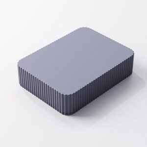 May include: A rectangular, light purple box with a fluted edge design. The box has a flat top and a ridged, vertical pattern around the sides. The overall shape is a simple, modern design.