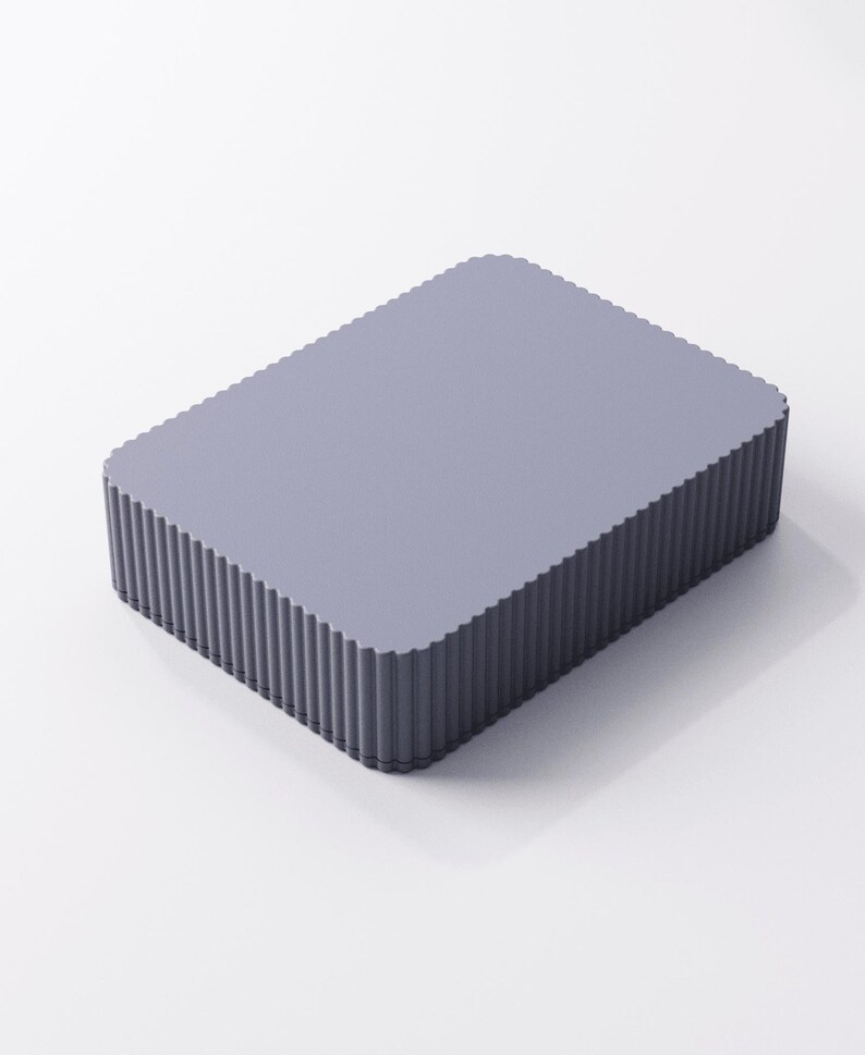 May include: A rectangular, light purple box with a fluted edge design. The box has a flat top and a ridged, vertical pattern around the sides. The overall shape is a simple, modern design.