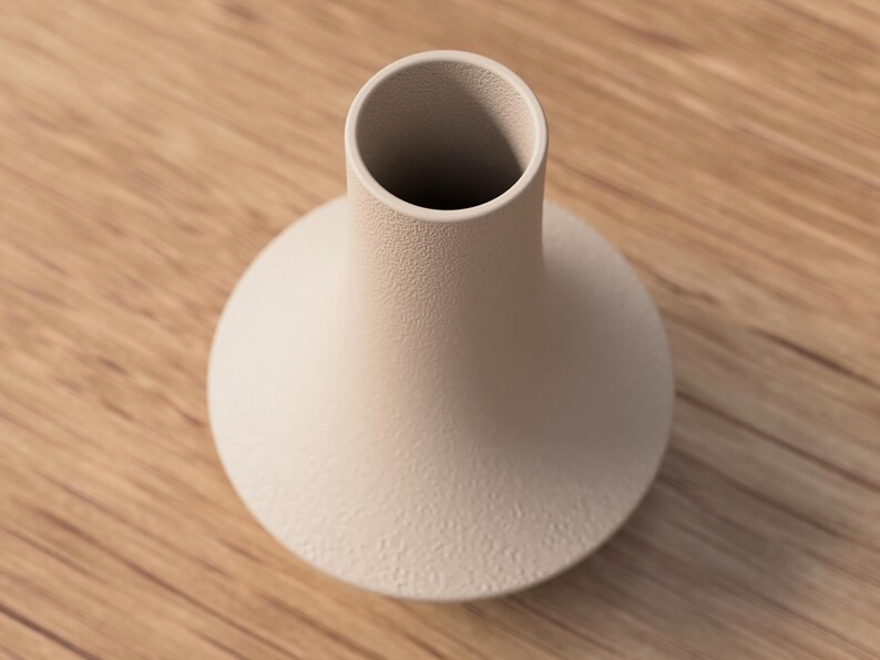 May include: A beige ceramic vase with a textured surface. The vase has a rounded base and a cylindrical neck. The vase is sitting on a wooden surface.