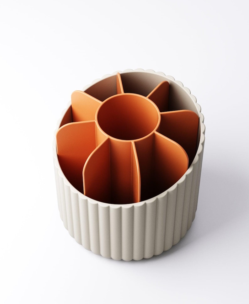 May include: A beige and orange desk organizer with a circular design. The organizer has a beige, ridged exterior and an orange interior divided into multiple compartments. The central compartment is also orange. The organizer is designed to hold pens, pencils, and other office supplies.