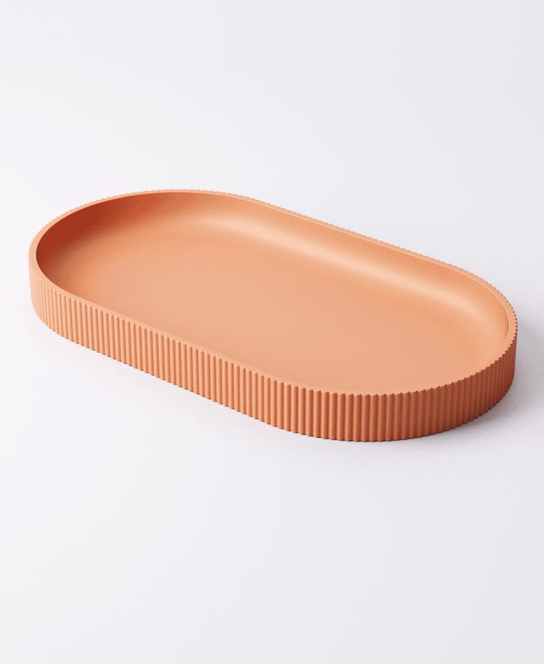 May include: A terracotta-colored, oval-shaped tray with a ribbed edge. The tray has a smooth interior and a textured, vertical-lined exterior. The design is minimalist and modern, suitable for serving or display.