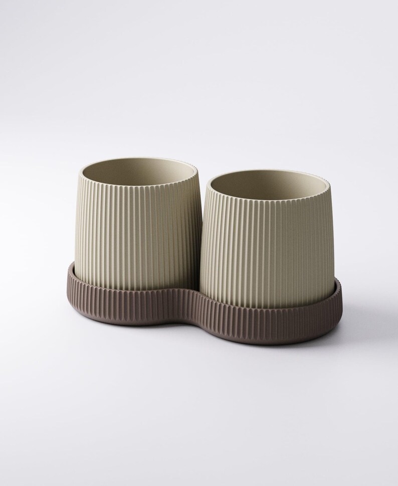 May include: Two beige cylindrical containers with vertical ribbed detailing, set on a brown, wavy-edged base. The containers have a minimalist design, suitable for holding items like pens or small plants. The neutral color palette offers a modern aesthetic.