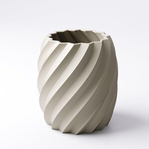 May include: A beige, cylindrical vase with a spiral design. The vase has a textured surface and a jagged top edge. The design features a series of diagonal, curved lines that wrap around the vase, creating a sense of movement.