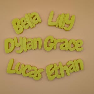 May include: Lime green foam name cutouts spelling "Bella", "Lilly", "Dylan Grace", "Lucas", and "Ethan". The names are in a rounded font, set against a light peach backdrop.