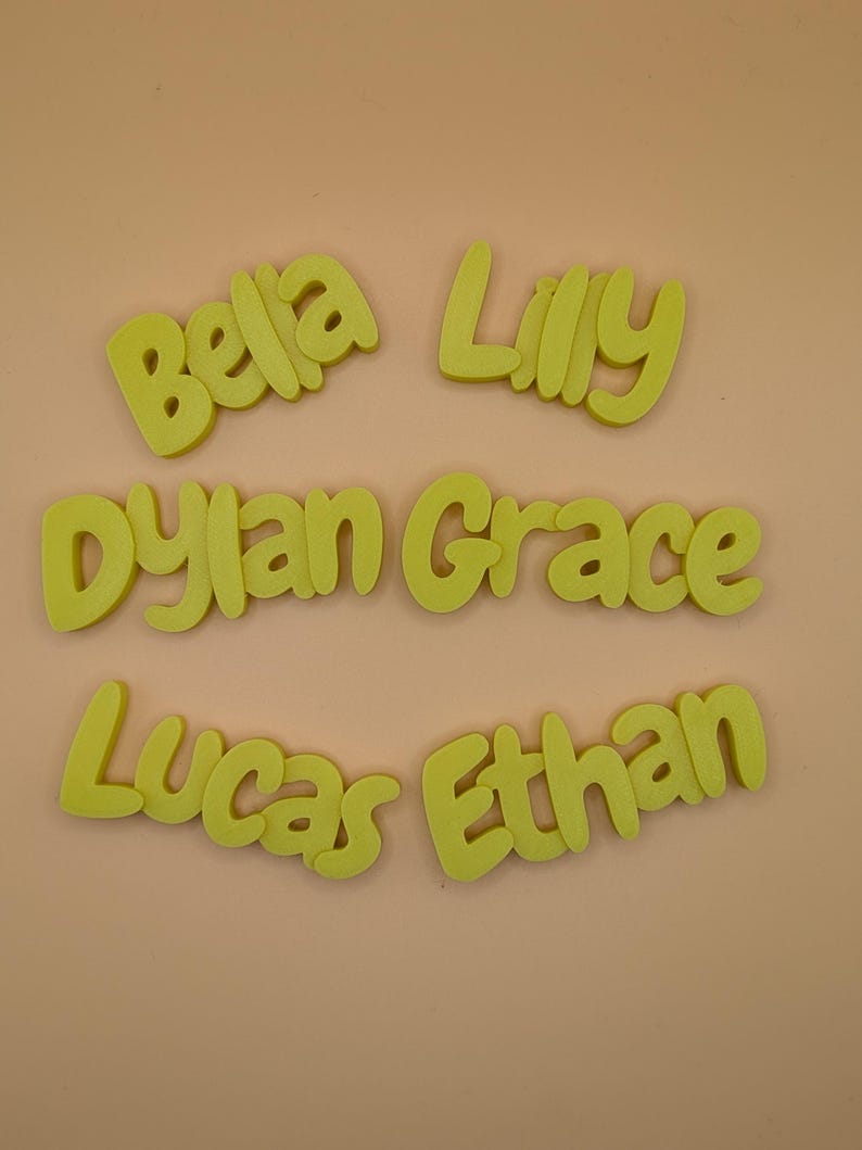 May include: Lime green foam name cutouts spelling "Bella", "Lilly", "Dylan Grace", "Lucas", and "Ethan". The names are in a rounded font, set against a light peach backdrop.