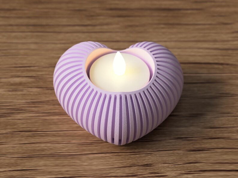 May include: A heart-shaped, lavender candle holder with vertical grooves. The holder contains a lit, white candle. The candle holder is on a wooden surface.