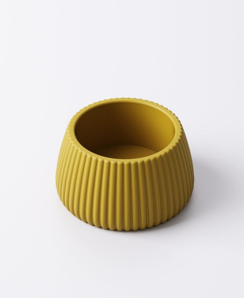 May include: Mustard yellow ceramic bowl with vertical ribbed detailing. The bowl has a rounded shape with a slightly flared base and a smooth interior. The rim has a subtle, textured edge. This decorative bowl is suitable for various uses.