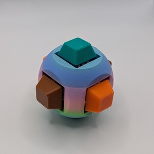 May include: A colorful 3D-printed puzzle toy. The spherical shape features a gradient of blue, pink, and green. It has six cube-shaped pieces in teal, brown, and orange. The toy is designed with a unique, geometric aesthetic.