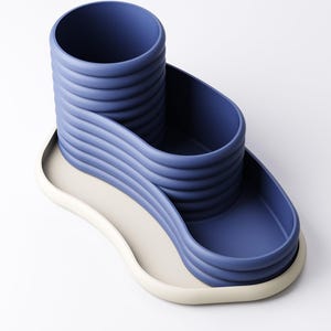 May include: A modern desk organizer in a minimalist design. The organizer is a deep blue color with a cylindrical pen holder and a wavy tray. The base is a light beige color. The design is made of a smooth, solid material.