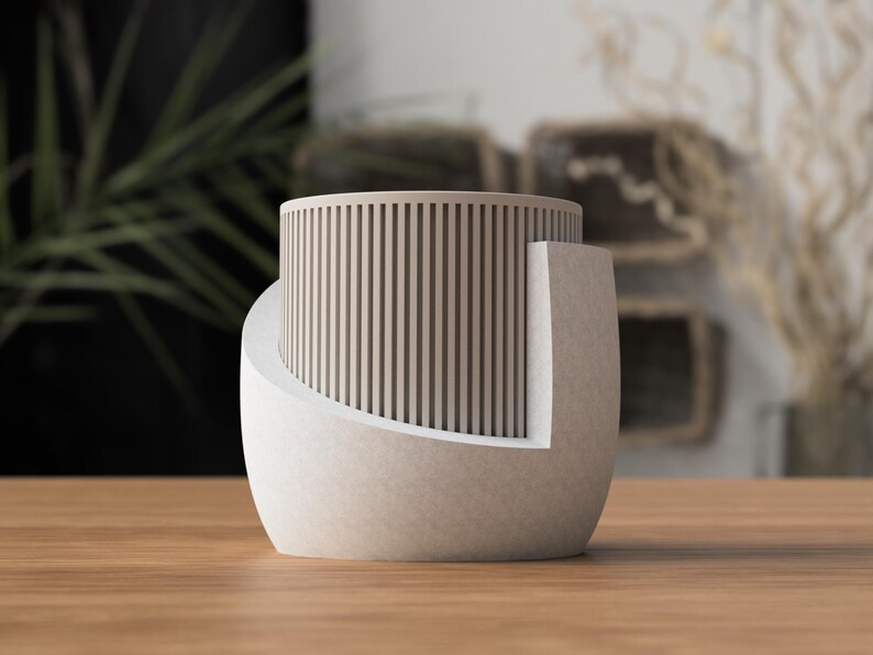 May include: A modern, beige-colored decorative object with a cylindrical top featuring vertical wooden slats. The base is a curved, solid form. The object sits on a wooden surface, with blurred background elements.