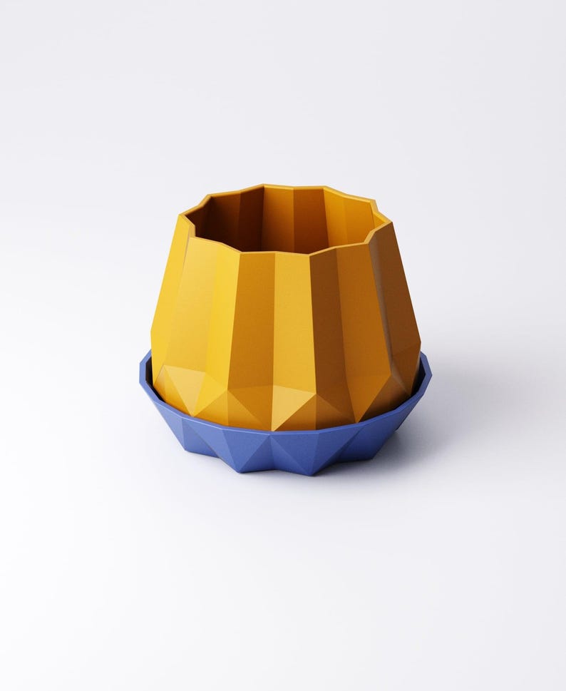May include: A geometric, yellow planter with a faceted design, sitting on a blue, similarly designed saucer. The planter has a wide, open top and a textured surface. The design is modern and minimalist.