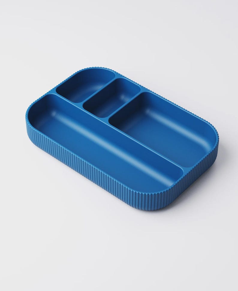 May include: A blue plastic divided tray with four compartments. The tray has a ribbed exterior and rounded corners. The compartments are different sizes, suitable for organizing small items. The tray is a solid, vibrant blue color.