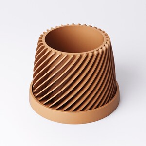 May include: A terracotta-colored planter with a unique spiral design. The planter has a cylindrical shape with vertical, curved ridges that create a textured surface. It sits on a matching saucer, suitable for indoor or outdoor use.