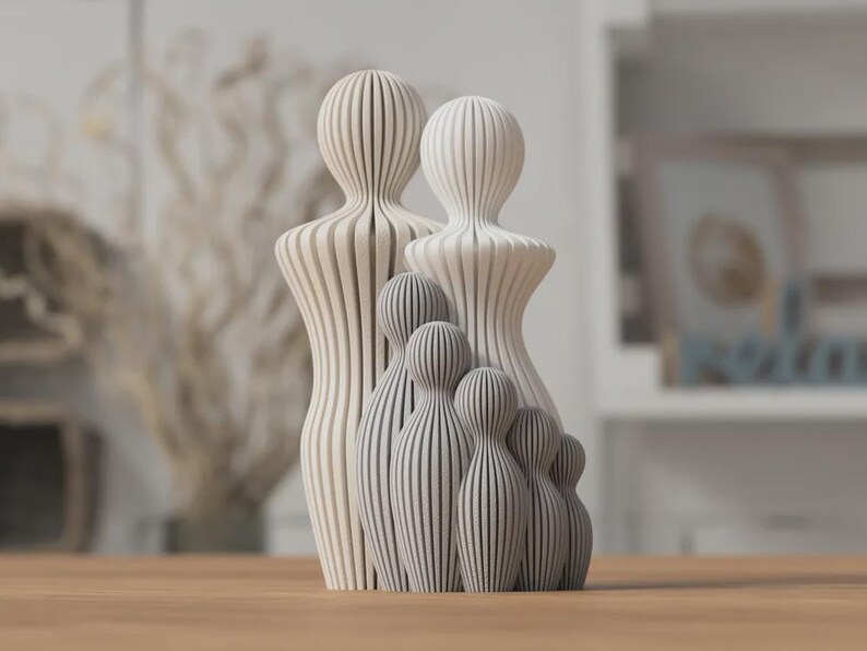 Puede incluir: Una escultura familiar de madera con un dise&ntilde;o minimalista. La escultura presenta dos figuras grandes y cuatro figuras m&aacute;s peque&ntilde;as, todas con un patr&oacute;n de rayas. Las figuras son en tonos de blanco y gris, y est&aacute;n dispuestas sobre una superficie de madera.