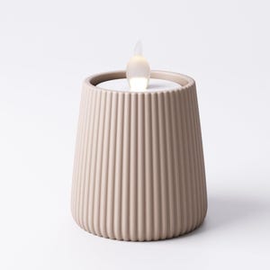 May include: A beige, ribbed candle holder with a flickering LED flame. The candle holder has a cylindrical shape with vertical grooves and a flat top. The LED flame is white and shaped like a teardrop.