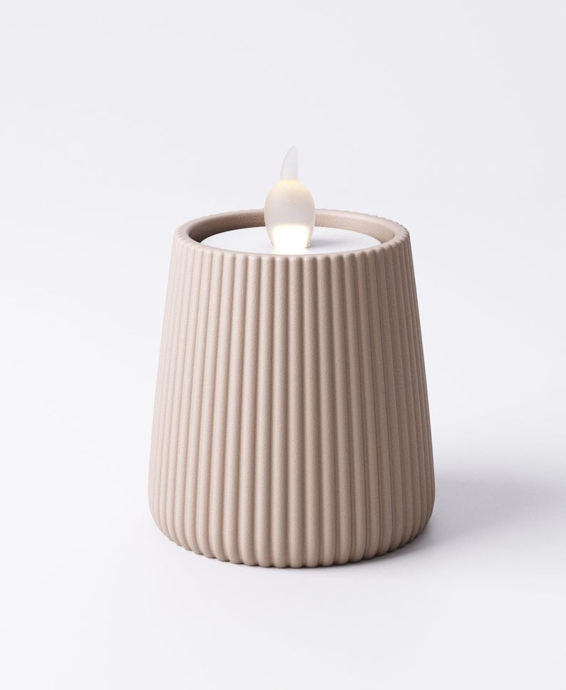 May include: A beige, ribbed candle holder with a flickering LED flame. The candle holder has a cylindrical shape with vertical grooves and a flat top. The LED flame is white and shaped like a teardrop.
