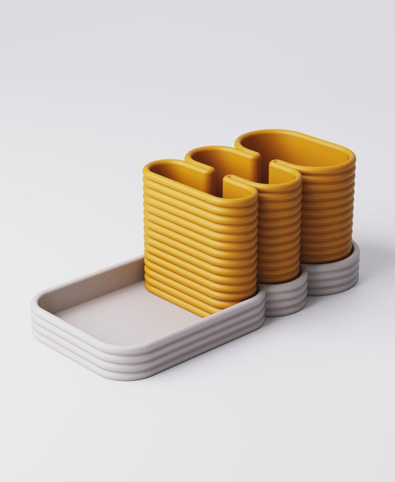 Puede incluir: Dise&ntilde;o moderno y abstracto con tres estructuras amarillas en forma de U, acanaladas, sobre una base gris, con una bandeja rectangular a juego. Los objetos tienen una est&eacute;tica minimalista y est&aacute;n sobre un fondo blanco.