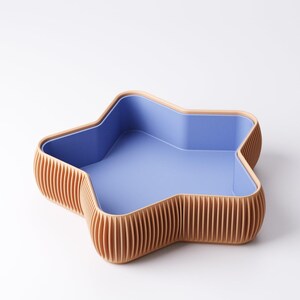 May include: A star-shaped decorative bowl with a light blue interior and a ribbed, tan exterior. The bowl has a smooth, light blue interior and a contrasting tan rim. The exterior features vertical, evenly spaced ribs.
