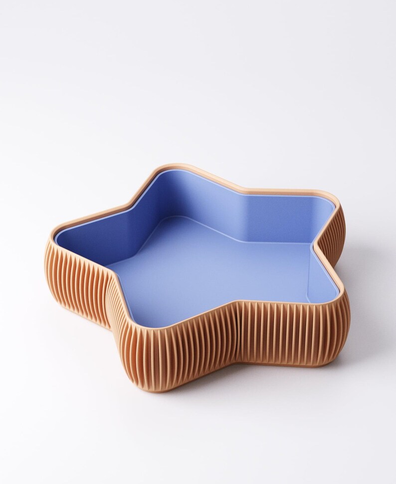May include: A star-shaped decorative bowl with a light blue interior and a ribbed, tan exterior. The bowl has a smooth, light blue interior and a contrasting tan rim. The exterior features vertical, evenly spaced ribs.