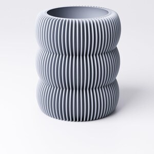 May include: A gray, cylindrical vase with a ribbed, vertical design. The vase has a wide opening at the top and a rounded base. The color is a muted gray, and the texture appears to be smooth.