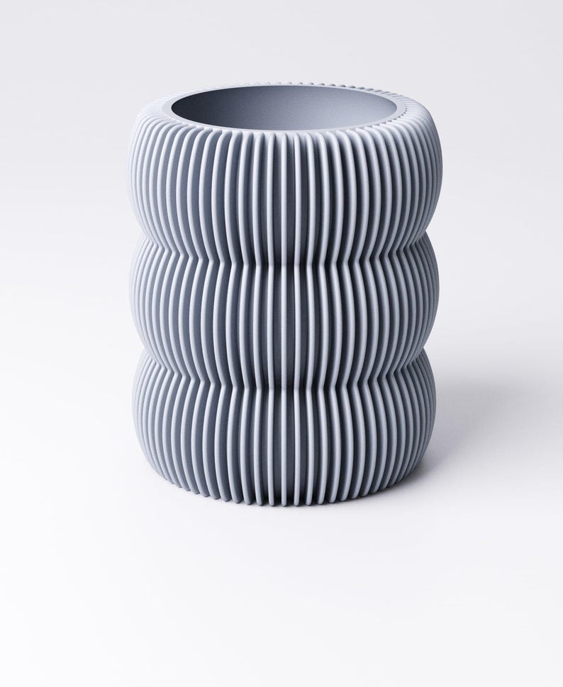 May include: A gray, cylindrical vase with a ribbed, vertical design. The vase has a wide opening at the top and a rounded base. The color is a muted gray, and the texture appears to be smooth.