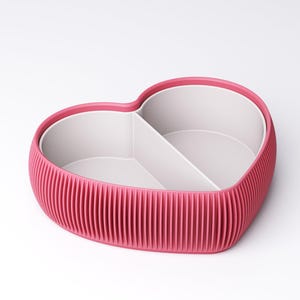 May include: A heart-shaped container with a ribbed, magenta exterior and a white interior divided into two sections. The rim is a darker shade of magenta. The container is designed for storage or organization.