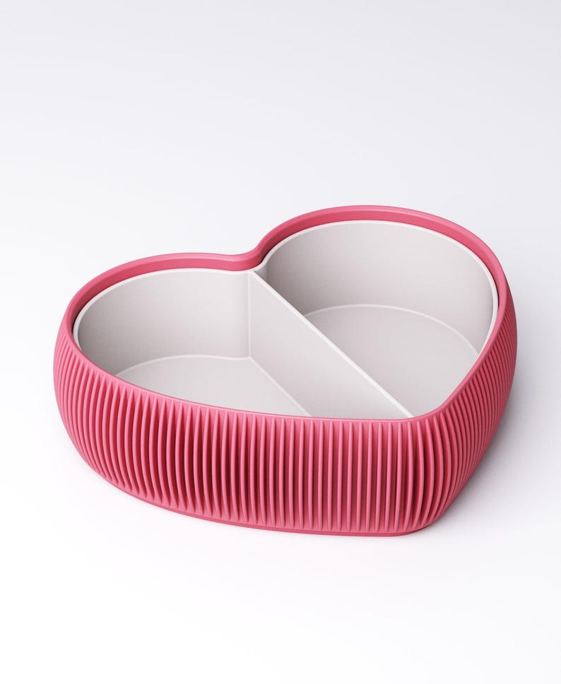 May include: A heart-shaped container with a ribbed, magenta exterior and a white interior divided into two sections. The rim is a darker shade of magenta. The container is designed for storage or organization.