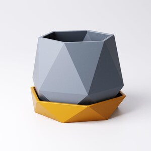May include: A geometric planter in shades of gray and yellow. The gray planter has a faceted design and sits atop a matching yellow saucer. The planter is designed with a modern aesthetic, suitable for small plants or succulents.