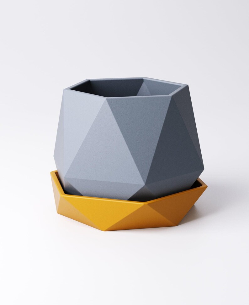 May include: A geometric planter in shades of gray and yellow. The gray planter has a faceted design and sits atop a matching yellow saucer. The planter is designed with a modern aesthetic, suitable for small plants or succulents.