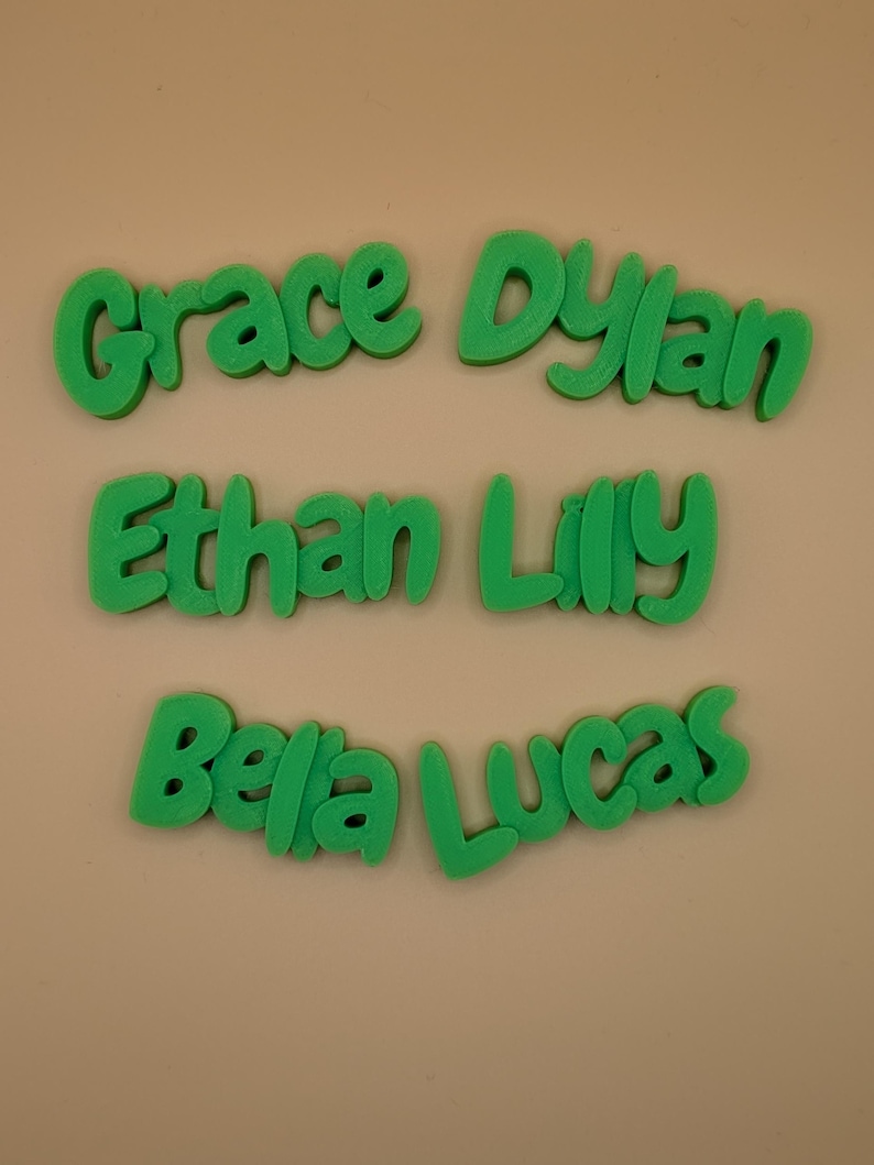 May include: Green 3D printed names: Grace, Dylan, Ethan, Lilly, Bella, and Lucas. The names are in a playful, rounded font, and are arranged on a neutral background. Suitable for personalized gifts or room decor.